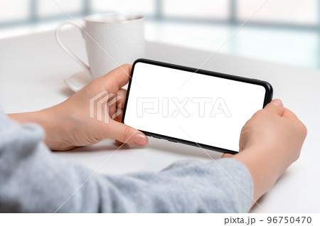 mockup cellphone horizontal position. Mockup image of woman holding black mobile phone with blank screen with coffee cup on table. Closeup of woman hand holding smartphone horizontal position 96750470