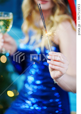 a woman with champagne and sparkler fire by Christmas tree. selective focus a woman with champagne and sparkler fire by Christmas tree. selective focus 96751953