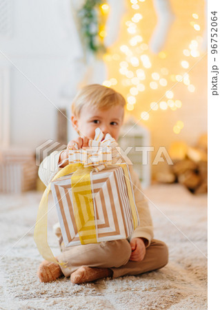 cute little boy with a gift in a box on the carpet in a room with a garland.  96752064
