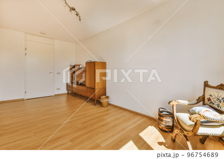 Modern cupboard and vintage chest placed near doors and wicker basket in spacious room with white walls and wooden floor 96754689