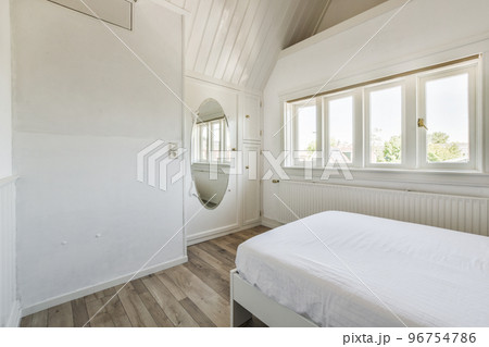 Modern home interior design of small mansard bedroom with white walls and soft cozy bed in daylight 96754786