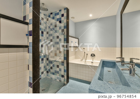 Sinks with mirrors, toilet and clean bathtub located near shower box with glass door in modern bathroom with white tiled walls Sinks with mirrors, toilet and clean bathtub located near shower box with glass door in modern bathroom with white tiled walls 96754854