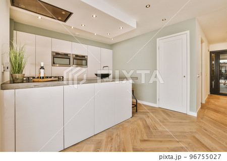 Contemporary minimalist style interior design of light studio apartment with wooden table and chairs in dining zone between open kitchen and living room with white walls and parquet floor 96755027