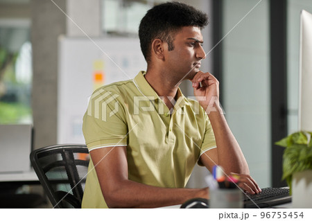 Pensive frowning UX designer working at office desk, answering e-mails from clients Pensive frowning UX designer working at office desk, answering e-mails from clients 96755454