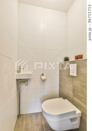 Wall hung toilet and small sink in corner in lavatory room with white and beige tile Wall hung toilet and small sink in corner in lavatory room with white and beige tile 96755753