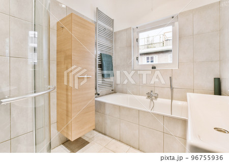 Sinks with mirrors and clean bathtub located near shower box with glass door in modern bathroom with white tiled walls 96755936