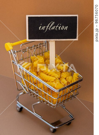INFLATION text on Blackboard label against Shopping trolley cart Filled With Pasta on Beige background. Food and groceries shopping price increase, Rising food cost food crisis inflation 96756070
