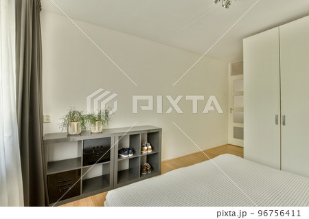 Comfortable bed with blanket placed near window and wardrobe in light bedroom 96756411