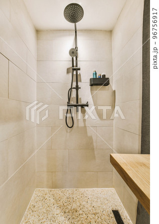 Shower faucets attached to tiled wall near glass partition and ornamental curtail in washroom at home 96756917