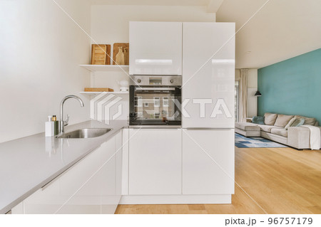 Fragment of interior of light narrow home kitchen with minimalist style white furniture with sink and stove Fragment of interior of light narrow home kitchen with minimalist style white furniture with sink and stove 96757179