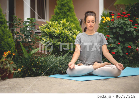 Concentrated woman sitting in lotus position yoga at summer garden park plants and blossom flowers 96757518