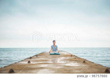 Yoga woman meditation in lotus position at pebble sea beach sunset sky horizon healthy lifestyle 96757660