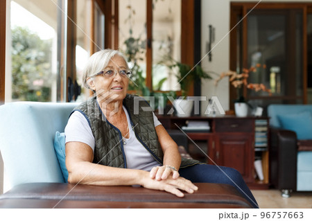Happy woman relaxing on her couch at home in the sitting room. Portrait of beautiful mature woman smiling while sitting at sofa at home. Beautiful senior woman smiling 96757663