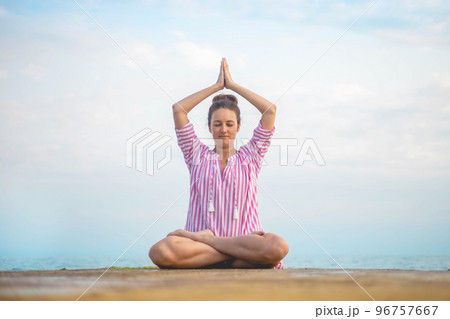 Yoga woman meditation prayer hands namaste overhead lotus position sitting sand sky beach landscape 96757667