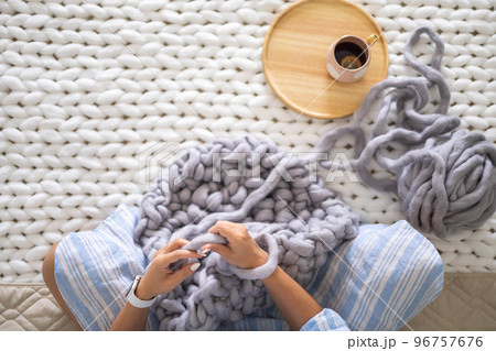 Female hands knitting warm plaid merino wool ribbon yarn sitting on bed hot tea top view closeup Female hands knitting warm plaid merino wool ribbon yarn sitting on bed hot tea top view closeup 96757676