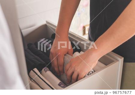 Closet male wardrobe dresser drawer neatly folded cotton sweatshirt t shirt Japanese storage method. Men's hands close-up. 96757677