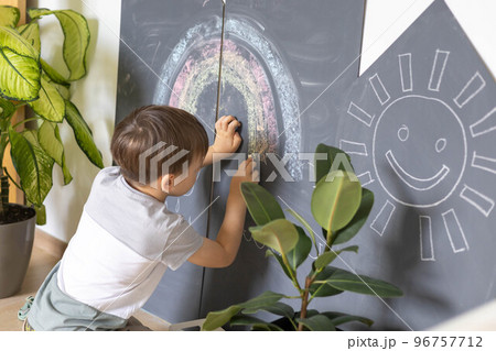 Cute baby boy drawing on black chalkboard colorful chalks indoor at childish playroom kindergarten 96757712