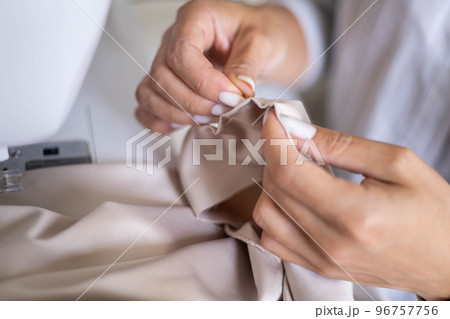 Female tailor hands sewing beige textile with needle and thread process of clothes handmade creating 96757756