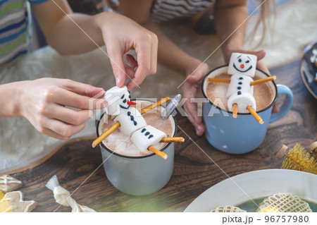 Little cute children eats a marmmello snowman decorated with icing and drinks cocoa. 96757980