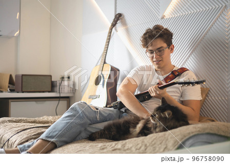 Cute cat relaxing near male playing electric guitar art hobby on couch at home Cute cat relaxing near male playing electric guitar art hobby on couch at home 96758090