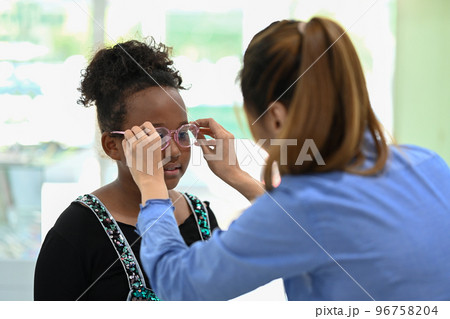 Cute little girl testing new glasses with optometrist in optical store. Eyesight and vision concept Cute little girl testing new glasses with optometrist in optical store. Eyesight and vision concept 96758204