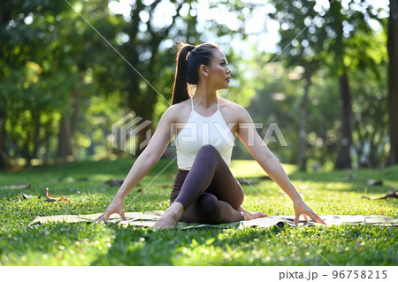 Elegant young woman in sportswear sitting in Half lord of the fishes pose, practicing yoga on green park with sunlight 96758215