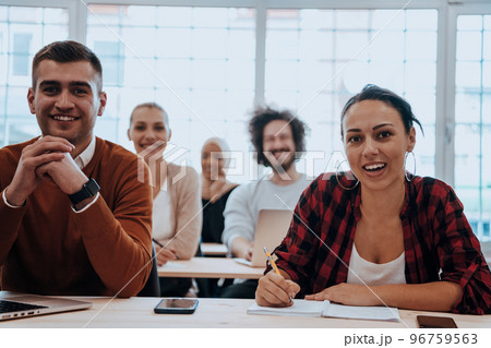 A group of diverse young men and women sit in a modern classroom and listen to a lecture on business training A group of diverse young men and women sit in a modern classroom and listen to a lecture on business training 96759563