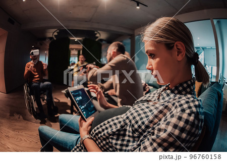 Pregnant woman sitting on the sofa of a modern office surrounded by colleagues and using a tablet Pregnant woman sitting on the sofa of a modern office surrounded by colleagues and using a tablet 96760158