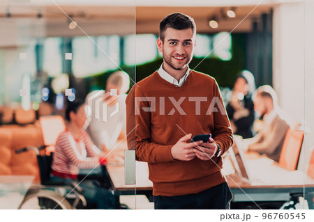 Handsome young business man standing confident in the office in front of his team Handsome young business man standing confident in the office in front of his team 96760545