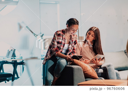 Two young women in a modern office solve a problem together while using a laptop Two young women in a modern office solve a problem together while using a laptop 96760606