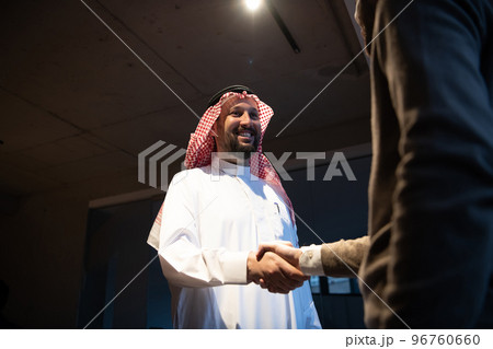 An elderly Arab man shaking hands with a businessman and ending a business meeting with successful business deals 96760660