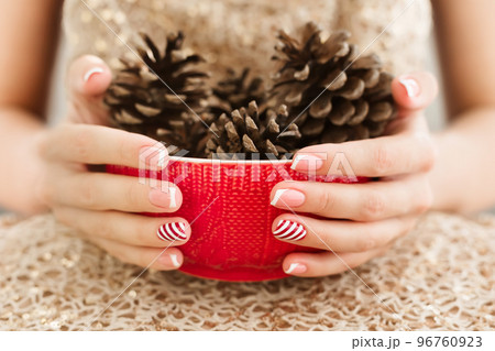 Woman's hands with french manicure and candy cane pattern on the nails. Woman with beautiful manicure holding big red knitted cup. The concept of cozy Christmas holidays and New Year. Woman's hands with french manicure and candy cane pattern on the nails. Woman with beautiful manicure holding big red knitted cup. The concept of cozy Christmas holidays and New Year. 96760923