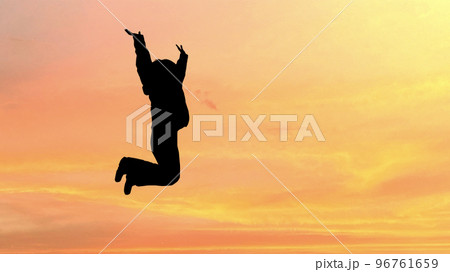 夕焼けにジャンプする女性のシルエット_ワイド 96761659