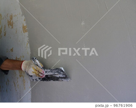 finishing leveling the surface of the room wall using a wide spatula, covering the wall with an even layer of putty with strong movements of the plasterer with a trowel in hand and space for text finishing leveling the surface of the room wall using a wide spatula, covering the wall with an even layer of putty with strong movements of the plasterer with a trowel in hand and space for text 96761906