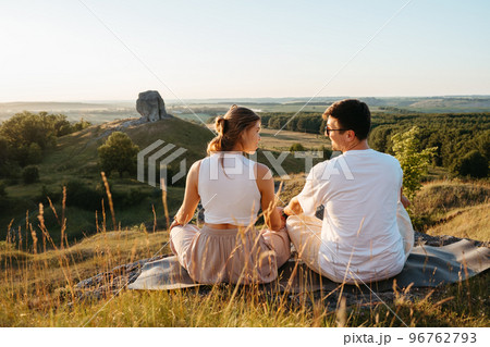 Man and Woman Practicing Yoga and Meditation Outdoors at Sunset with Scenic Landscape and Nature Miracle Giant Stone on the Background Man and Woman Practicing Yoga and Meditation Outdoors at Sunset with Scenic Landscape and Nature Miracle Giant Stone on the Background 96762793