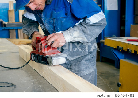 Professional woodworker grinds wooden bar on workbench in carpentry workshop with tool. Middle-aged Professional woodworker grinds wooden bar on workbench in carpentry workshop with tool. Middle-aged 96764781