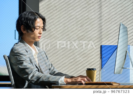 オフィスの窓辺で仕事をする若いビジネスマン オフィスの窓辺で仕事をする若いビジネスマン 96767323