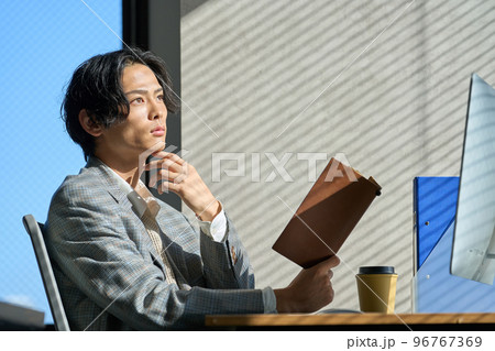 オフィスの窓辺で仕事をする若いビジネスマン オフィスの窓辺で仕事をする若いビジネスマン 96767369