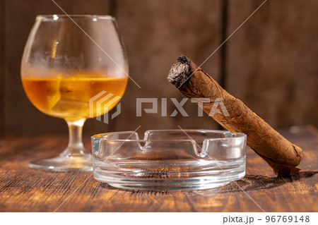 Glass of whisky and lighted cigar in an ash tray 96769148