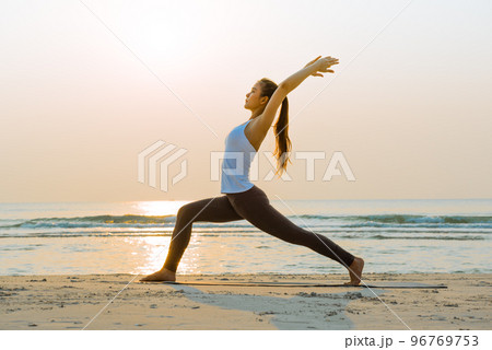 Young Asian woman doing Yoga exercise on the sand beach in the morning at sunrise. 96769753