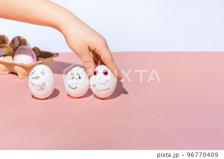 The child paints white eggs and puts them on a pink and white background. Funny and romantic faces drawn with a marker. Easter holiday concept. The child paints white eggs and puts them on a pink and white background. Funny and romantic faces drawn with a marker. Easter holiday concept. 96770409
