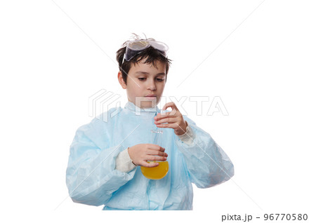 Smart teenage schoolboy in protective laboratory coat, conducts a scientific experiment in a chemistry lesson, using a glass rod, mixes reagents with chemicals in lab flask, isolated on white backdrop 96770580