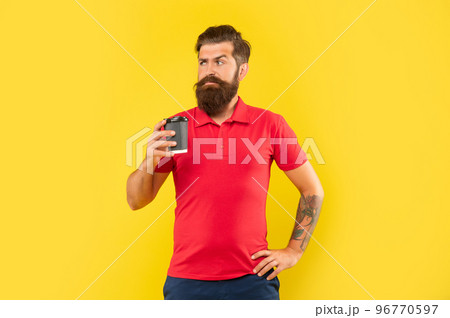 Serious bearded man in casual tshirt holding coffee cup with arm akimbo yellow background, takeaway 96770597