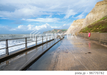 Big waves and water splashes at West Bay beach near Bridgport in Dorset, United Kingdom. Walkway or promenade along the beach, selective focus 96770782