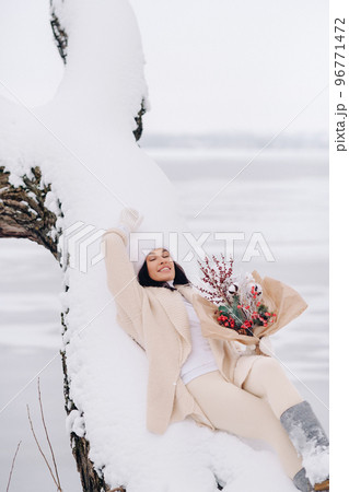 A beautiful girl in a beige cardigan and a white hat with flowers enjoys a snowy winter in nature 96771472
