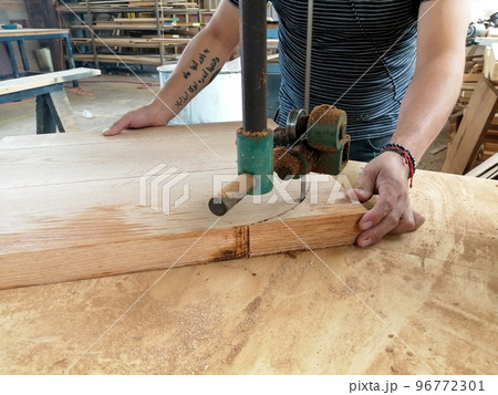 A man cuts wood on a circular saw in a joinery, band saw, holding a plank A man cuts wood on a circular saw in a joinery, band saw, holding a plank 96772301
