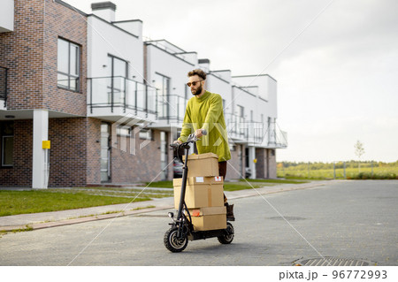 Man drives electric scooter with cardboard packages Man drives electric scooter with cardboard packages 96772993