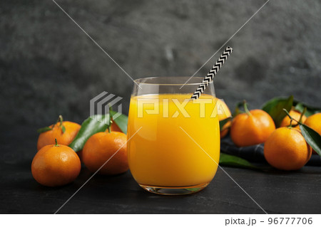 Glass of fresh tangerine juice and fruits on black table Glass of fresh tangerine juice and fruits on black table 96777706