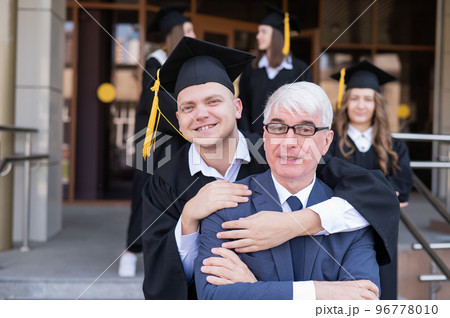 Father and son embrace at graduation. Parent congratulates university graduate. Father and son embrace at graduation. Parent congratulates university graduate. 96778010