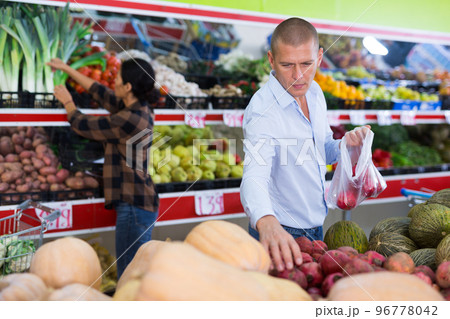 Focused man choosing pomegranates on counter in greengrocery store Focused man choosing pomegranates on counter in greengrocery store 96778042